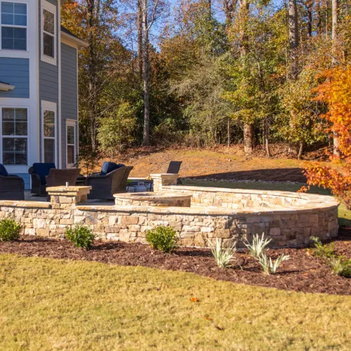 a backyard with a stone wall and a brick patio with a stone wall