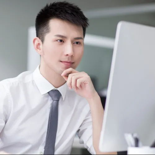 Young businessman in white shirt and gray tie focused on computer screen in modern office setting