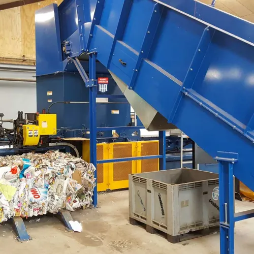 Industrial recycling machine compressing mixed paper waste into dense bales inside a processing facility.
