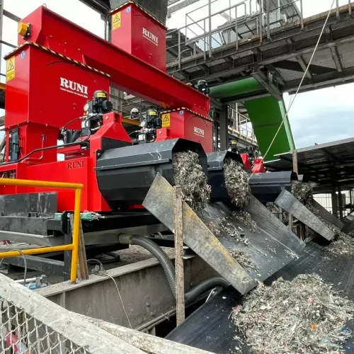 Industrial metal shredding machine processing scrap metal onto conveyor belts in recycling plant.