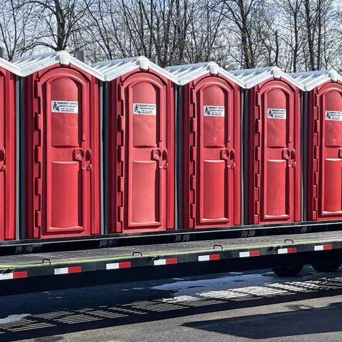 Row of red portable restrooms lined up on a trailer during a daylight setting.