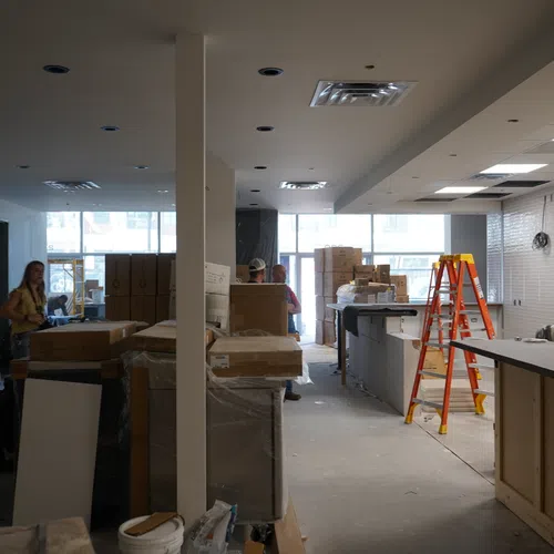 Interior of a commercial space under renovation with stacked boxes, tools, ladders, and workers inside.