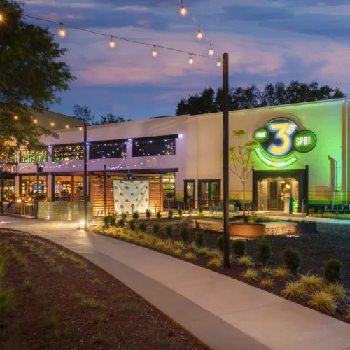Evening view of a brightly lit 3 Spot building with outdoor greenery, string lights, and a walkway.