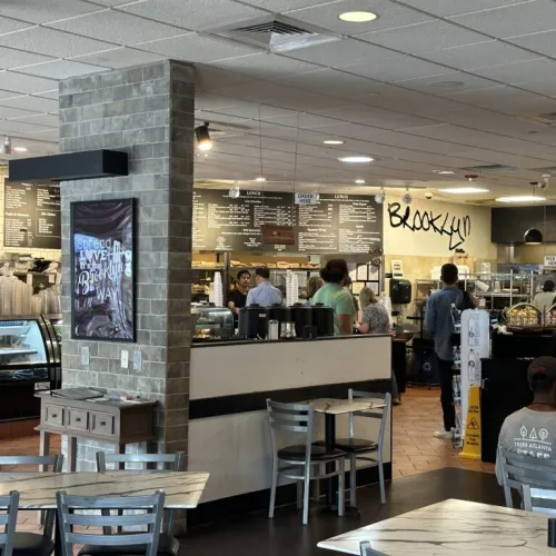 Busy Brooklyn cafe interior with customers, menu boards, modern decor, and seating area with tables and chairs.