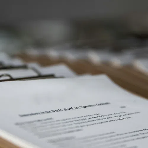 Close-up of stacked printed documents with metal binder clips on wooden table in soft focus background.