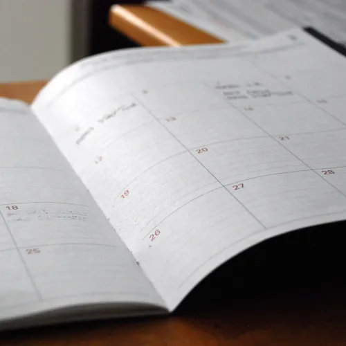 Open monthly planner calendar on wooden desk showing dated weekly layout for scheduling events and appointments.