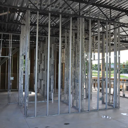 Interior of a building under construction with metal stud framing and exposed ceiling structure.