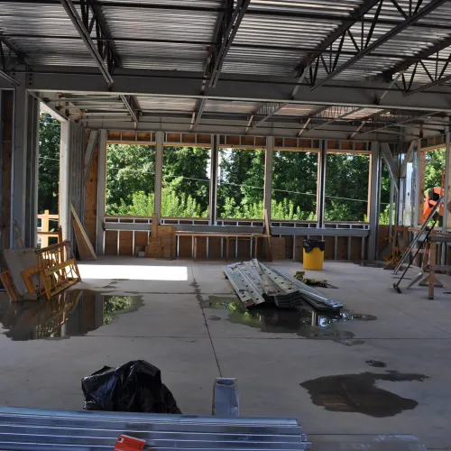 Interior of a steel-framed building under construction with workers in safety vests and helmets inspecting the site.