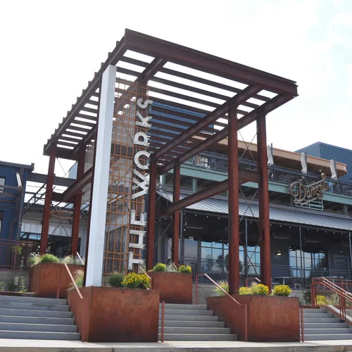 Modern industrial-style building entrance with steel beams and The Works signage on a sunny day.