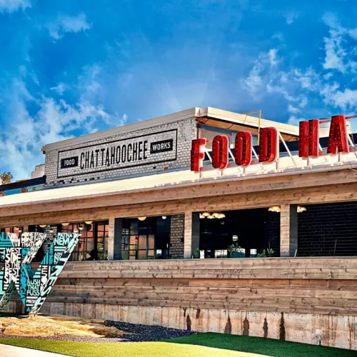 Exterior view of Chattahoochee Food Works Food Hall with clear sky and artistic signage on wooden facade.