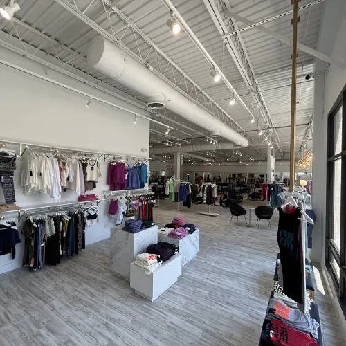 Bright clothing store interior with hanging outfits, folded clothes, modern fixtures, and large windows.