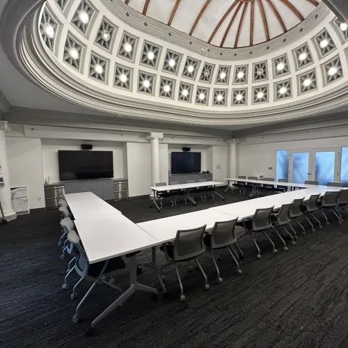 Modern conference room with U-shaped white tables, rolling chairs, and a decorative domed ceiling with lights.