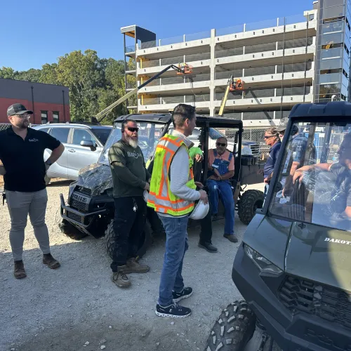 Construction workers gathered near utility vehicles at an urban building site on a sunny day.