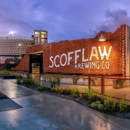 Scofflaw Brewing Co. exterior with brick wall signage and industrial surroundings at sunset.
