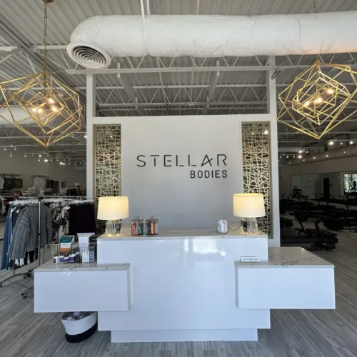 Modern fitness studio reception area with white desk, geometric light fixtures, and Stellar Bodies logo on wall