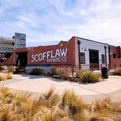Scofflaw Brewing Co. building with red brick exterior under a blue sky and landscaped grass in front.