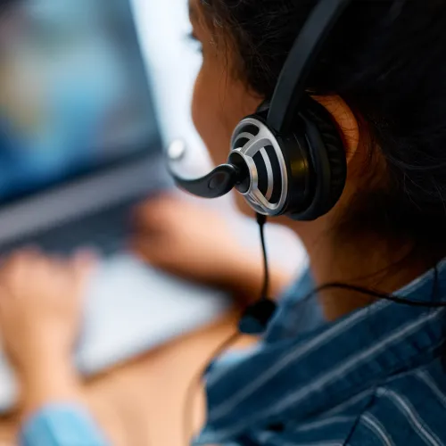 Person wearing headset working on a laptop, focused on online communication or virtual meeting.