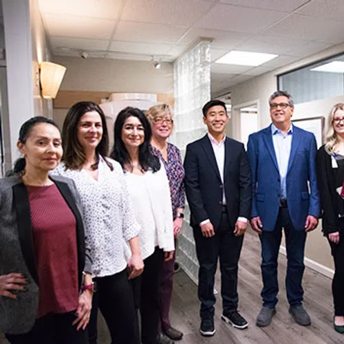 Group of nine diverse professionals standing in a modern office hallway smiling at the camera.