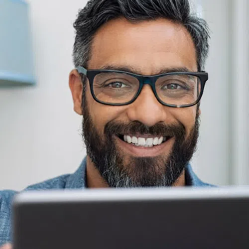 Happy man with glasses using a tablet in a modern indoor setting with a lamp in the background