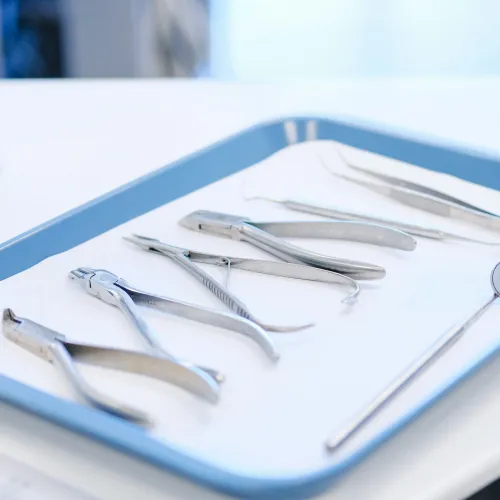 Tray displaying various stainless steel dental tools including mirror, forceps, and scalers on white paper.