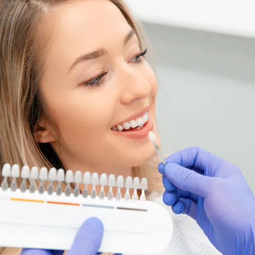 Dentist matching a tooth shade for a smiling woman using a dental shade guide in a clinic.