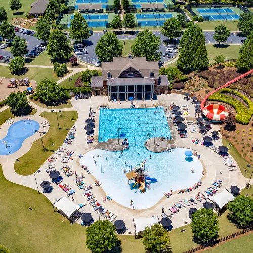Aerial view of a vibrant community pool area with water slides, playgrounds, tennis courts, and surrounding greenery.