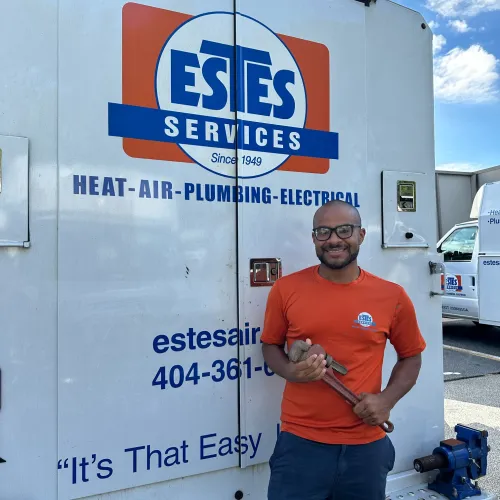 Estes Services Plumber  in orange shirt holding a pipe wrench standing next to an Estes Services branded truck with service information.