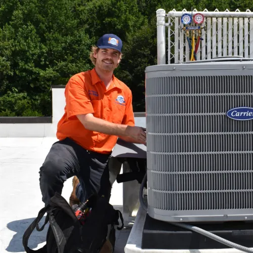 Estes Services Technician in orange uniform repairing a Carrier air conditioning unit on rooftop with tools in Alpharetta, Georgia