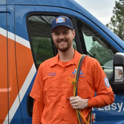 Estes Services Smiling technician in orange uniform holding cables beside branded Estes service van outdoors