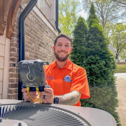 Estes Services Technician in orange shirt working on HVAC unit outside a residential home on a sunny day.