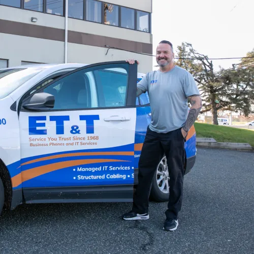 Man standing next to ET&T white and blue company vehicle outside office building on sunny day