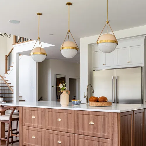 Modern kitchen island with wooden cabinets, white countertop, pendant lights, and stainless steel refrigerator.