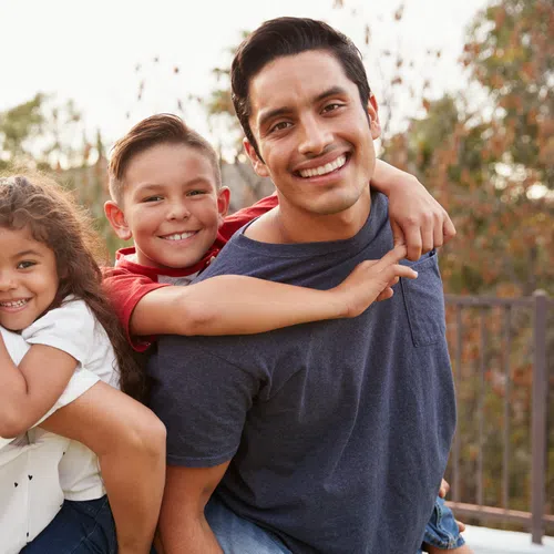 Happy family of four smiling outdoors with children hugging parents in a park setting during daytime