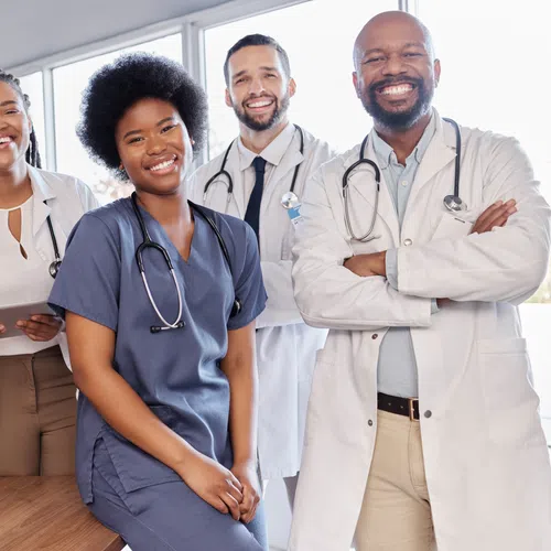 Smiling diverse group of five medical professionals in scrubs and lab coats with stethoscopes in bright office