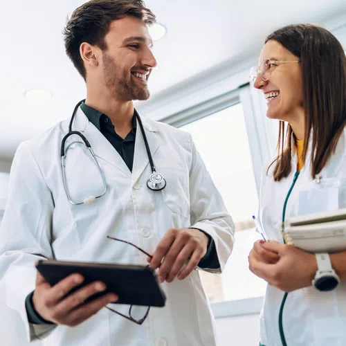 Male and female doctors smiling and discussing information in a bright modern clinic while holding medical records.