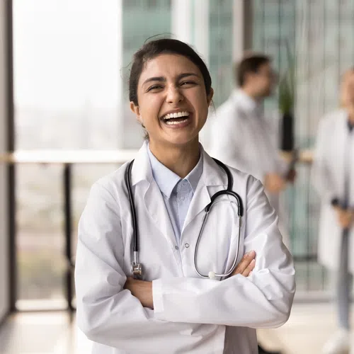 Smiling female doctor in a white coat with stethoscope in modern hospital corridor with colleagues.
