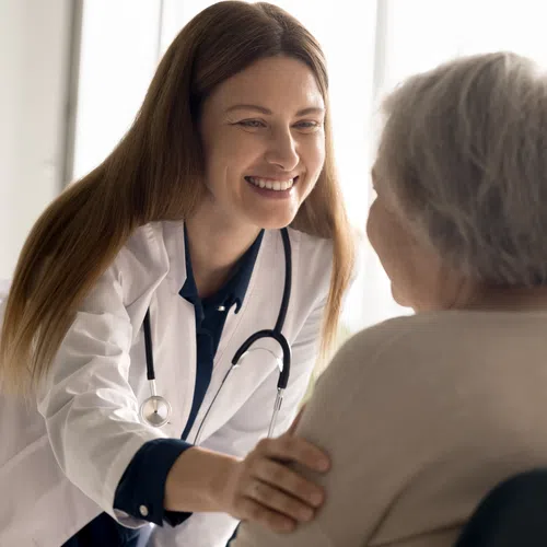 Smiling female doctor with stethoscope comforting elderly woman during a consultation in bright room