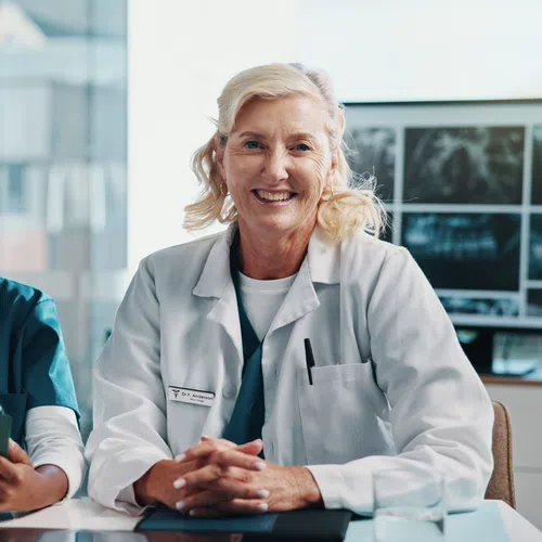 Two female healthcare professionals smiling in a medical office with X-rays in the background.