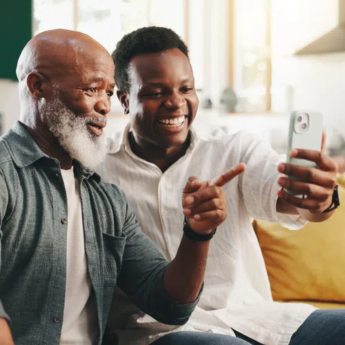 Smiling older man and young man sitting on couch taking a selfie together with smartphone in bright living room