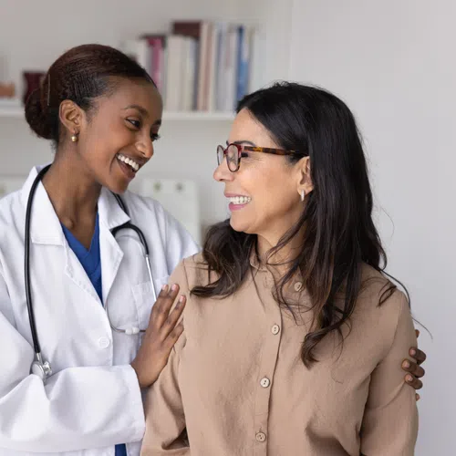 Smiling female doctor with stethoscope comforts and supports happy female patient in medical office.