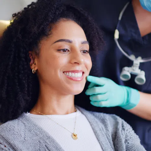 Smiling woman looking at her teeth in a mirror during a dental checkup with a masked dentist.