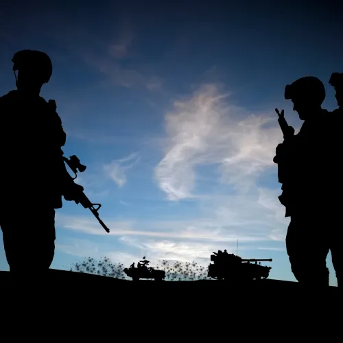 Silhouettes of soldiers with weapons against a blue sky during sunset on a hilltop.