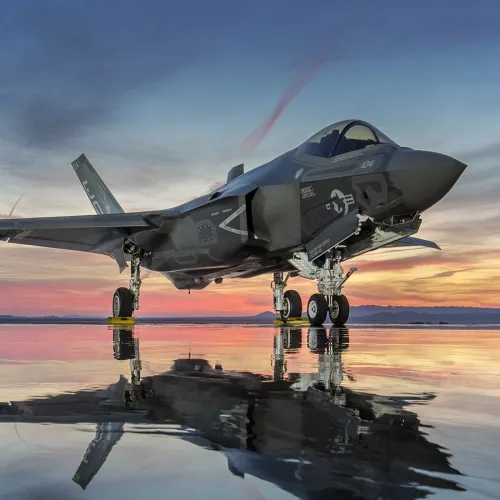 F-35 stealth fighter jet parked on reflective runway at sunset with vibrant sky and clouds.
