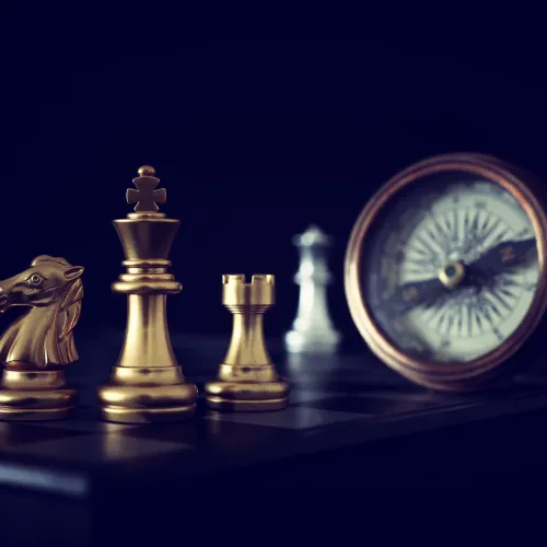 Golden chess pieces including knight, king, and rook on a board with a vintage compass in the background