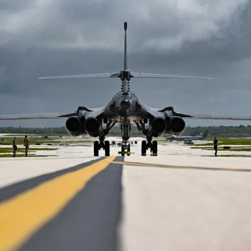 Rear view of a military bomber aircraft taxiing on a runway under a cloudy sky with crew around.