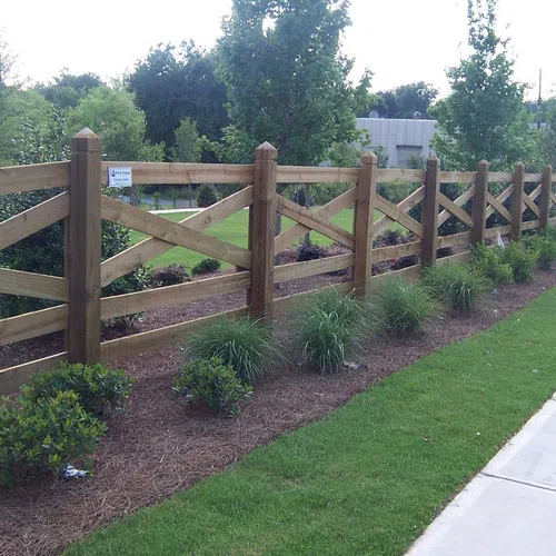 Wooden split-rail fence alongside a landscaped pathway with lush greenery and bushes.