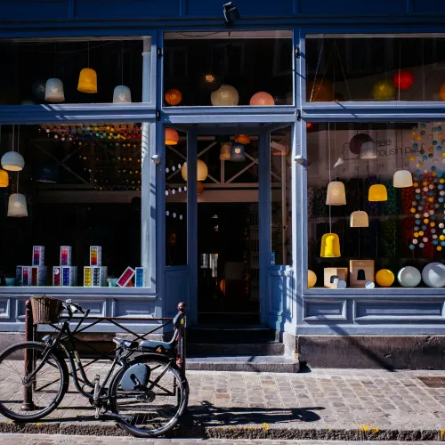 Blue storefront with hanging pendant lamps, colorful decor, and a bicycle parked on the cobblestone street outside