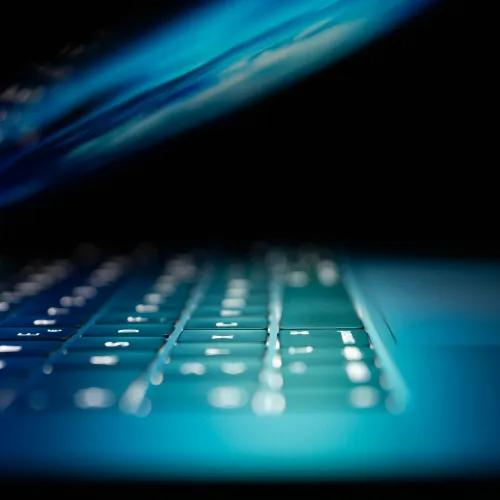 Close-up of a laptop keyboard with illuminated keys and blurred screen in low light environment.
