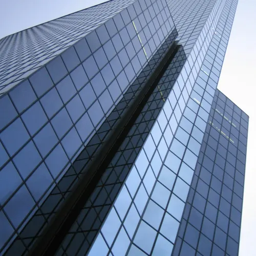Modern skyscraper with reflective glass windows towering against a clear sky, viewed from below.