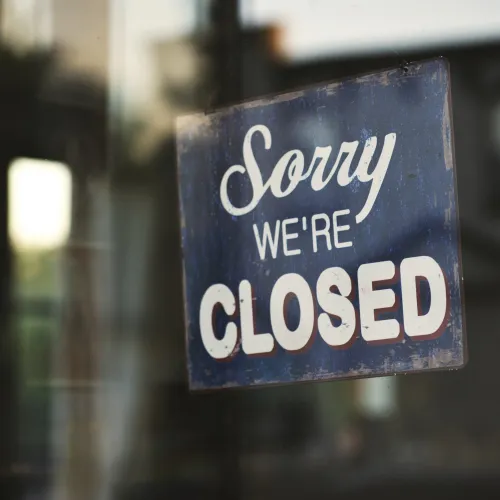 Blue sign on glass door reading Sorry We're Closed with a blurred background seen through the window